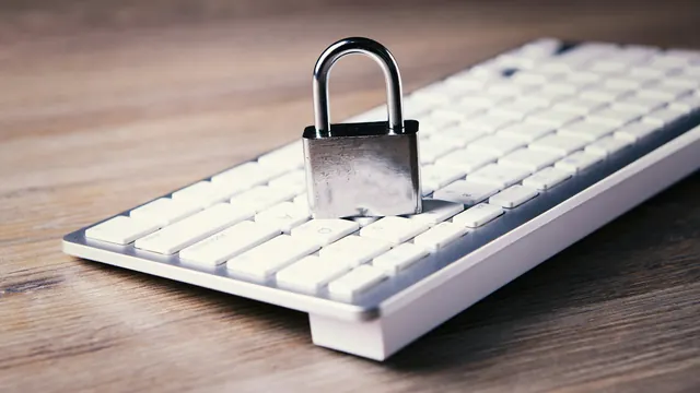 Zamknięta metalowa kłódka na białej klawiaturze komputerowej leżącej na drewnianym blacie