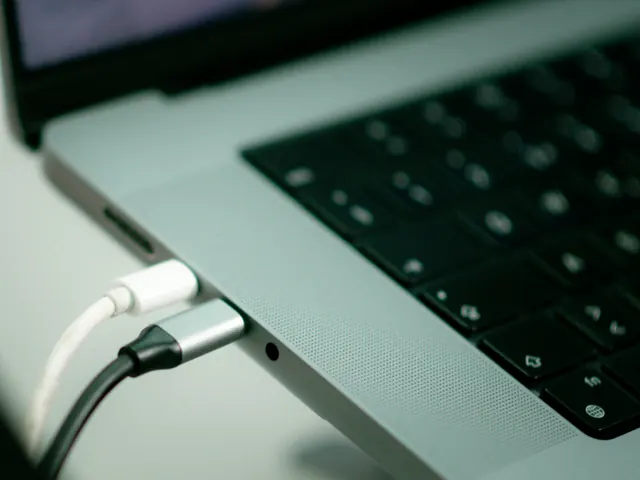 Dwa kable USB-C podłączone do boku srebrnego laptopa na jasnym biurku