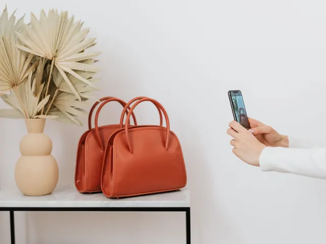 Dłonie trzymają smartfon i nagrywają dwie rude torebki na białym stoliku pod jasną ścianą