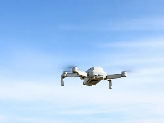 Mały biały dron w locie na tle jasnobłękitnego nieba z delikatnymi chmurami