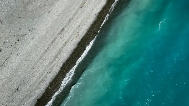 Widok z drona na jasną plażę i turkusowe morze przecięte ukośną linią brzegu